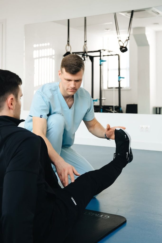 Fisioterapia Fénix Cádiz - Experienced physiotherapist helps patient stretch leg in a modern clinic setting, focusing on rehabilitation.